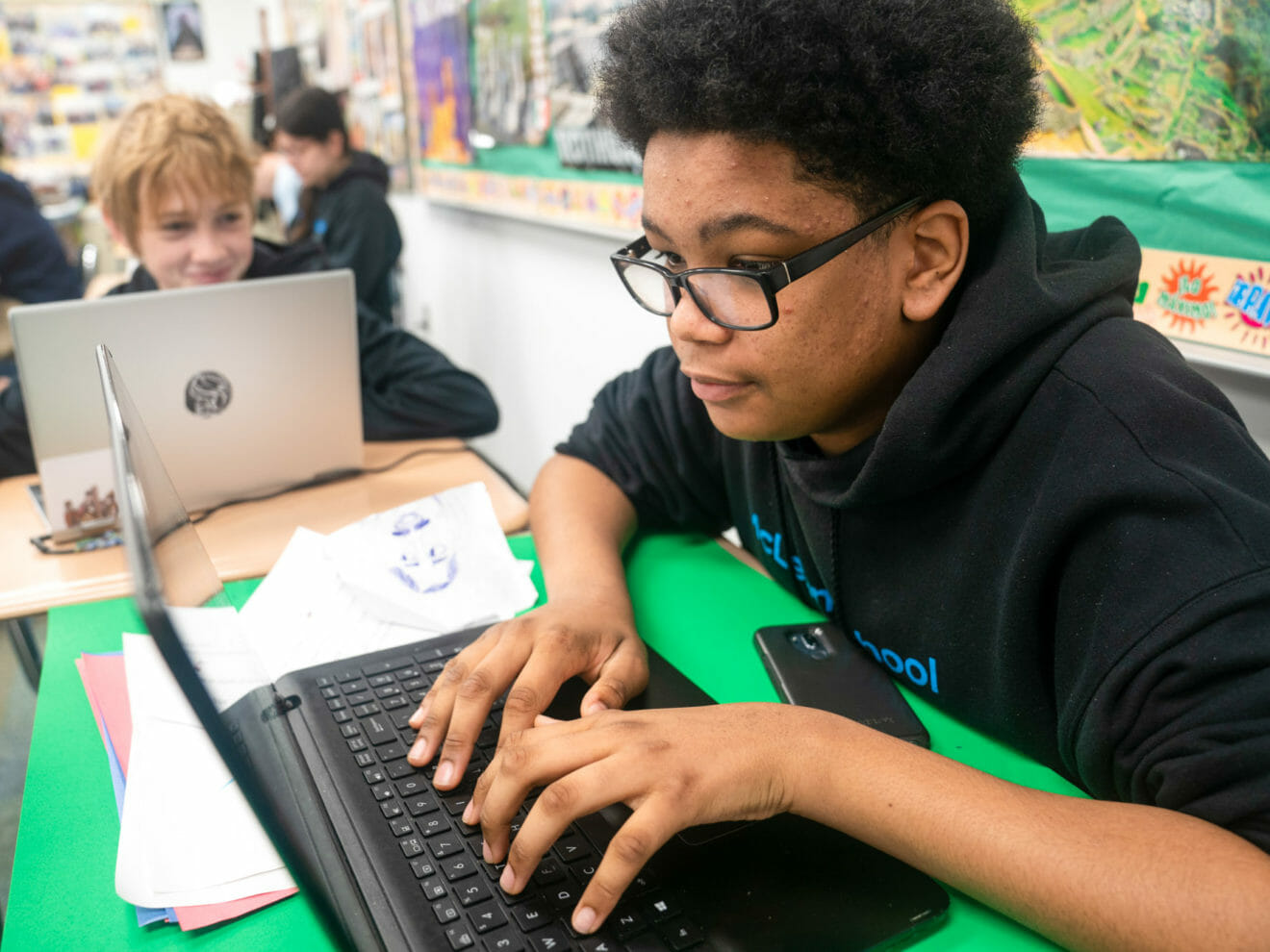 Boy in glasses uses laptop in class