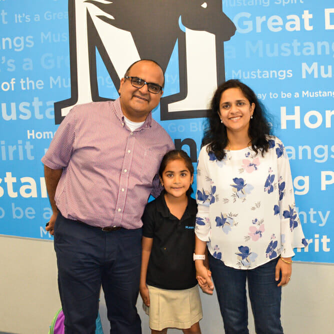 Parents and student stand in front of McLean School wall