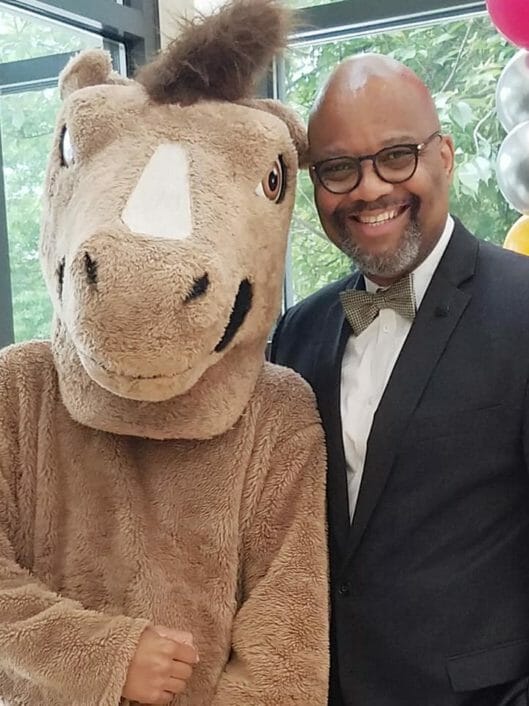 Bobby Edwards, the Director of Community Inclusion and External Relations at McLean, smiling while posing with McLean's Mustang mascot