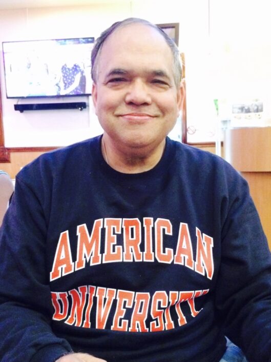 Rajiv Gupta, Assistant Accountant at McLean School, smiles in his American University sweatshirt